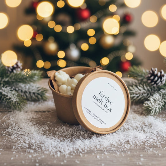 The festive melt box open with the lid half on. On top of a wood countertop with snow dust surrounding it, and a blurred Christmas Tree with lights in the background.