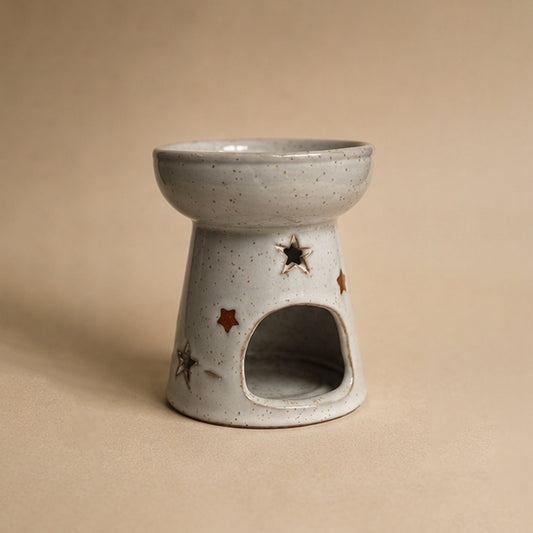 Ceramic wax burner with star designs on a beige background