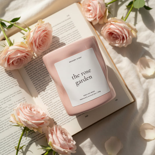 Pink candle labeled 'the rose garden' on an open book with pink roses around it.