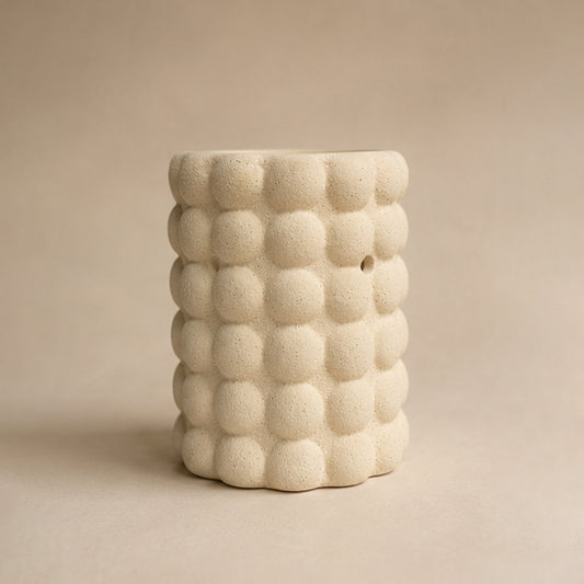 Cylindrical ceramic bubble wax burner with a textured, bubble-like surface on a beige background