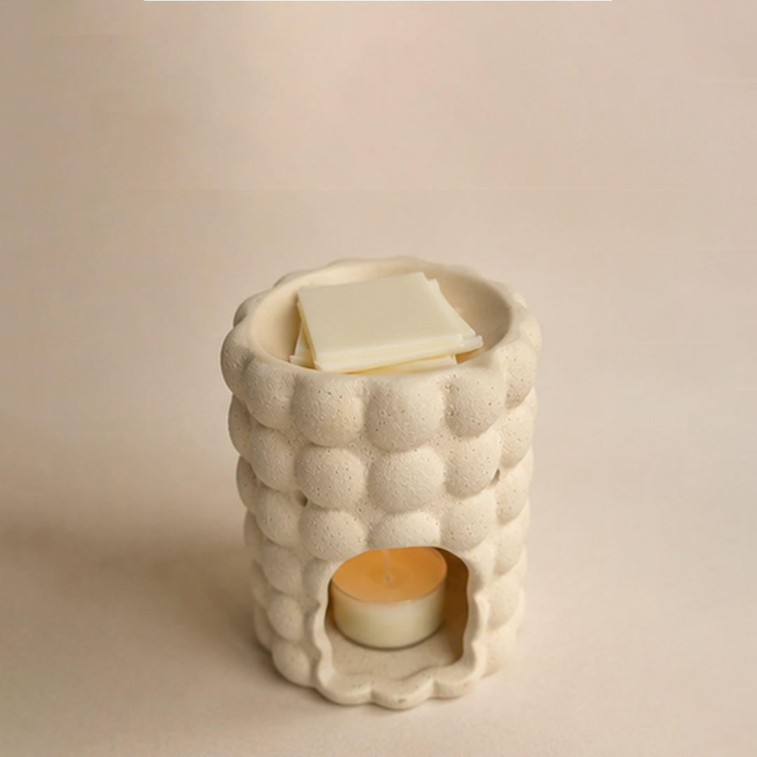 Ceramic wax burner with a tealight inside and wax melt blocks on a beige background