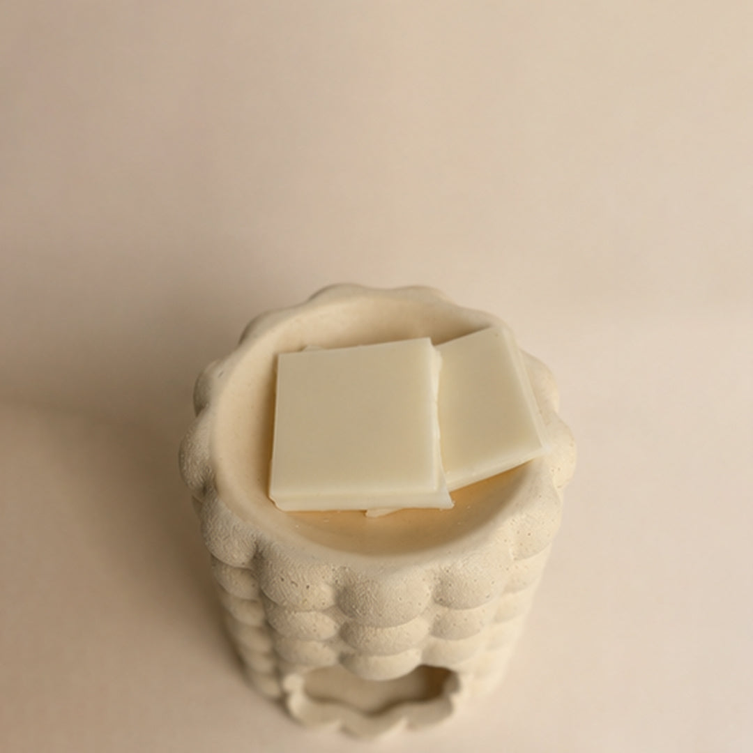 White wax melt blocks in a textured ceramic wax burner on a beige background