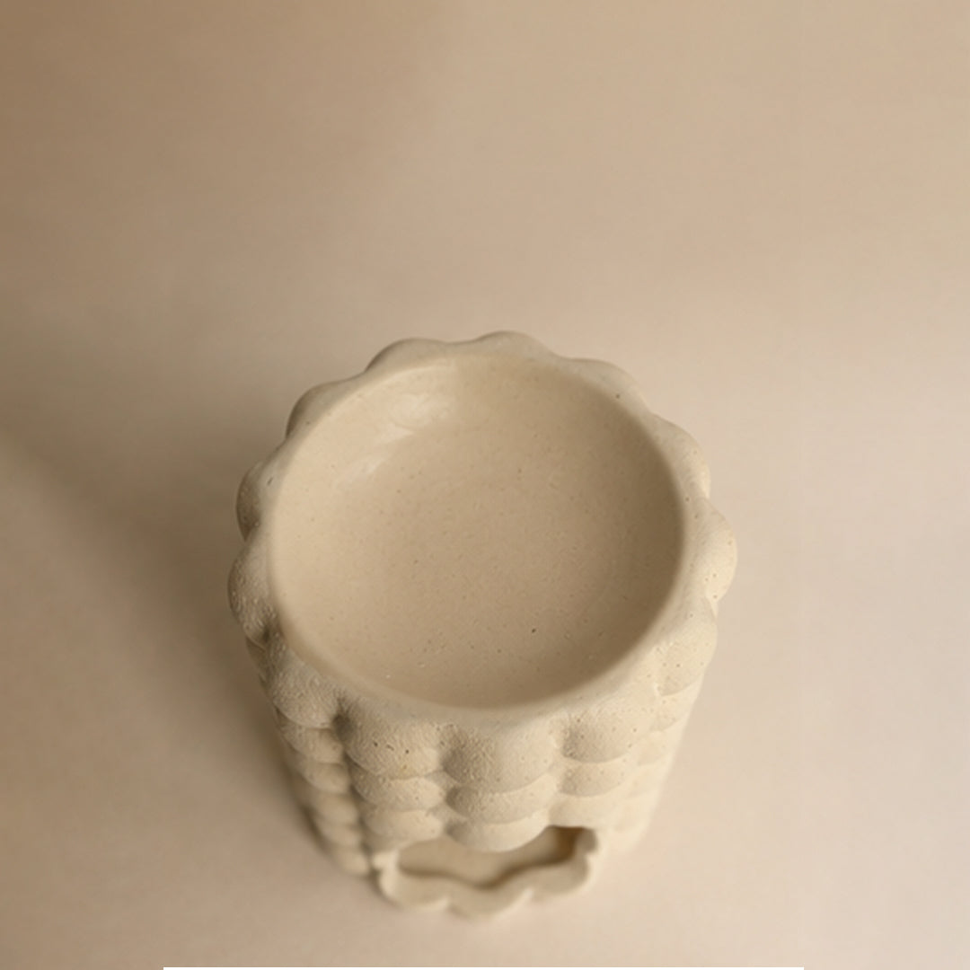Top view of a beige ceramic wax burner with textured design on a beige background