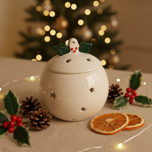 Christmas Pudding Wax Burner with a christmas themed background, christmas tree sparkling lights and holly leaves and orange slices.