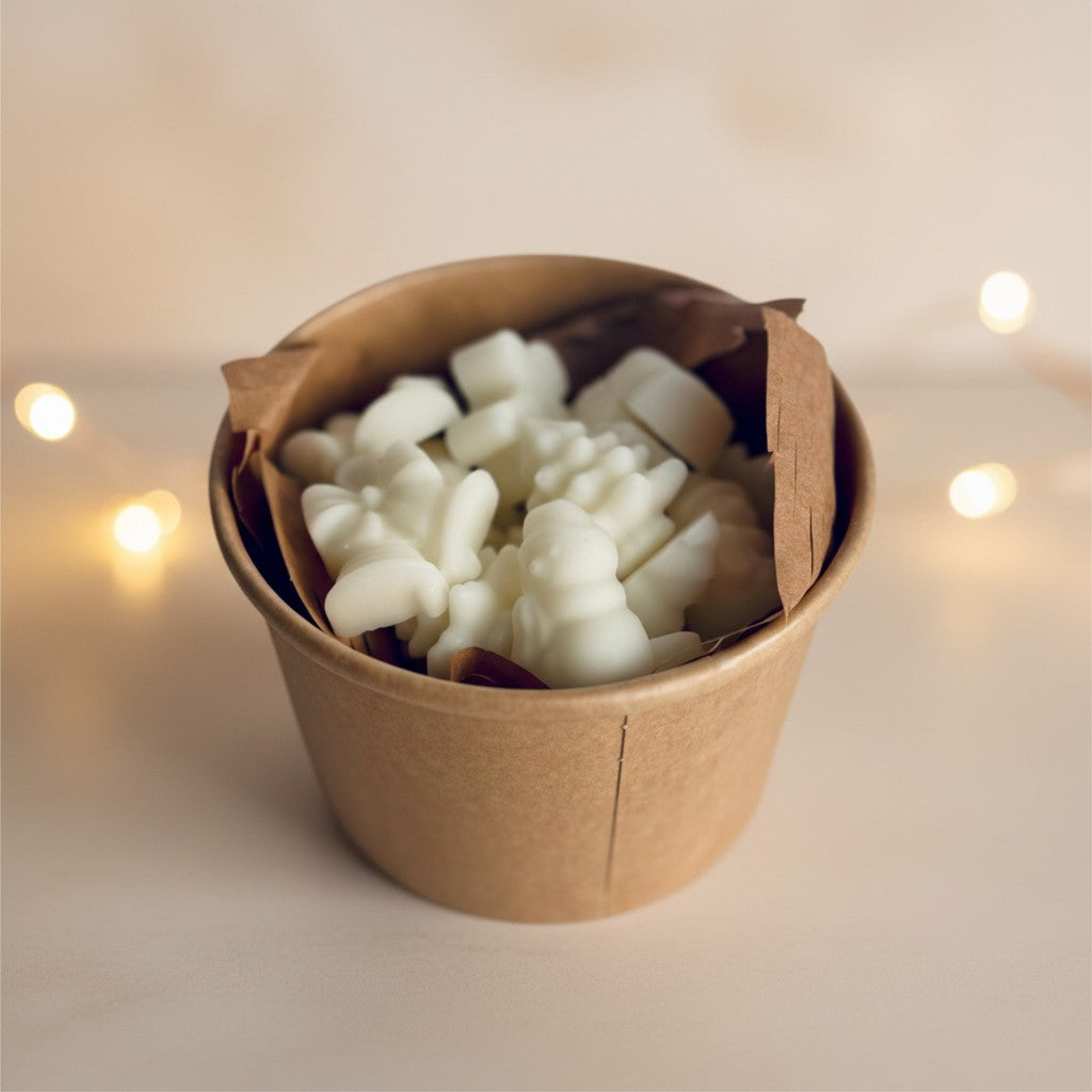 A box of the festive melt box open without the lid, showing the wax melts inside. Behind in the background are some blurres out fairy lights.