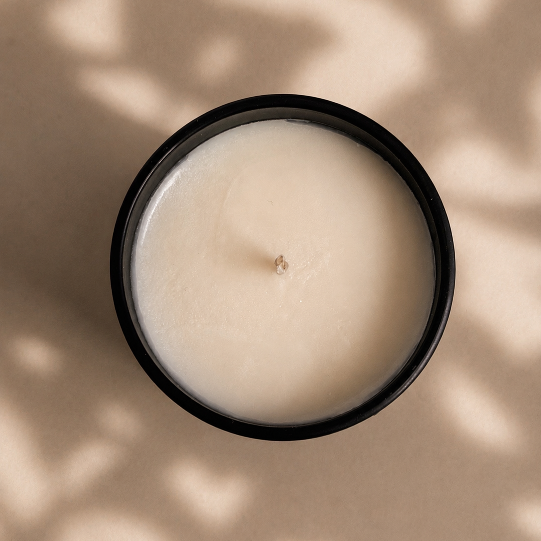 White candle in a black container on a beige surface with leaf shadows