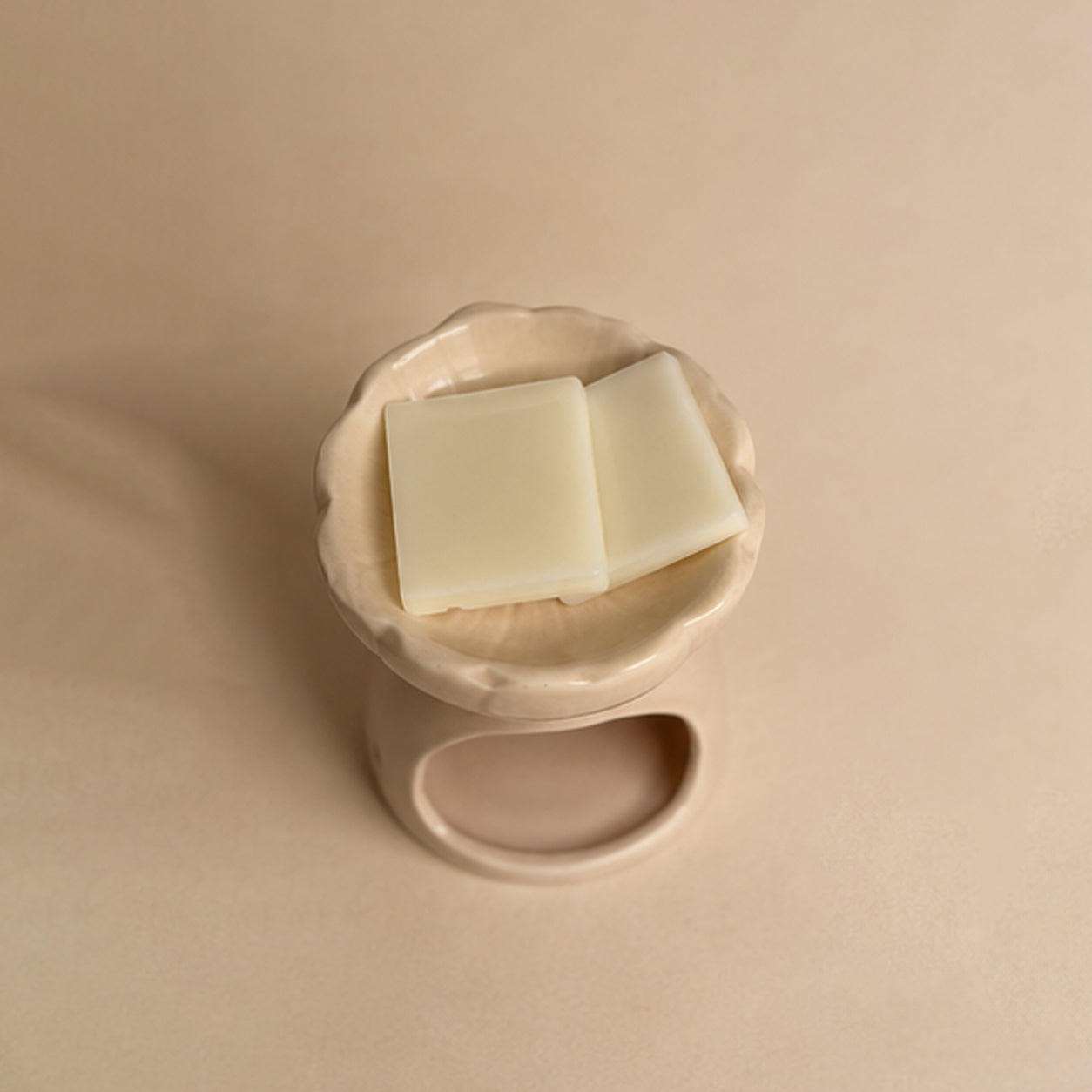 Pink blossom ceramic wax burner top down view on a beige plain background, with wax melt snap bar blocks in the top.