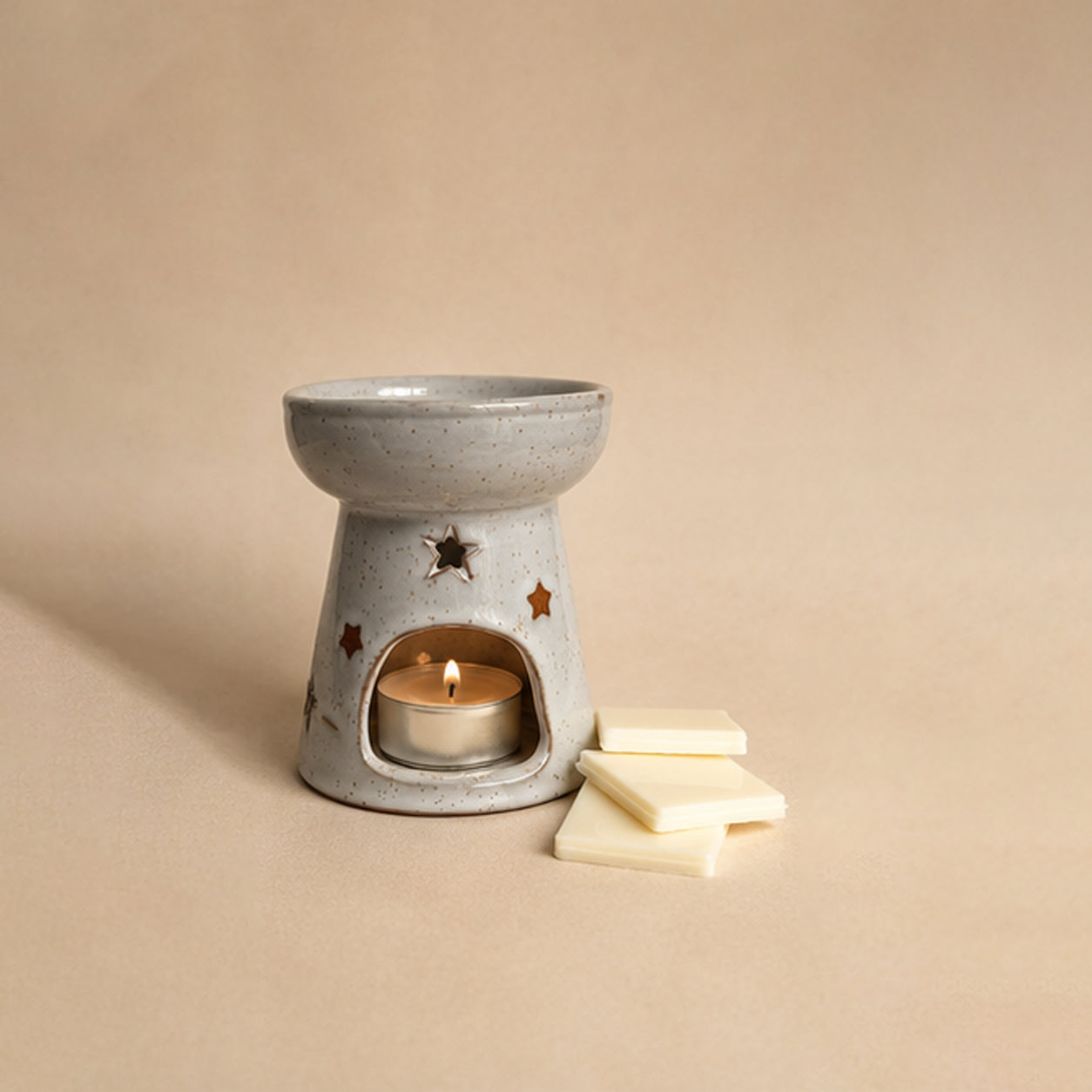 Ceramic wax burner with a lit candle and wax melt snap bars on a beige background