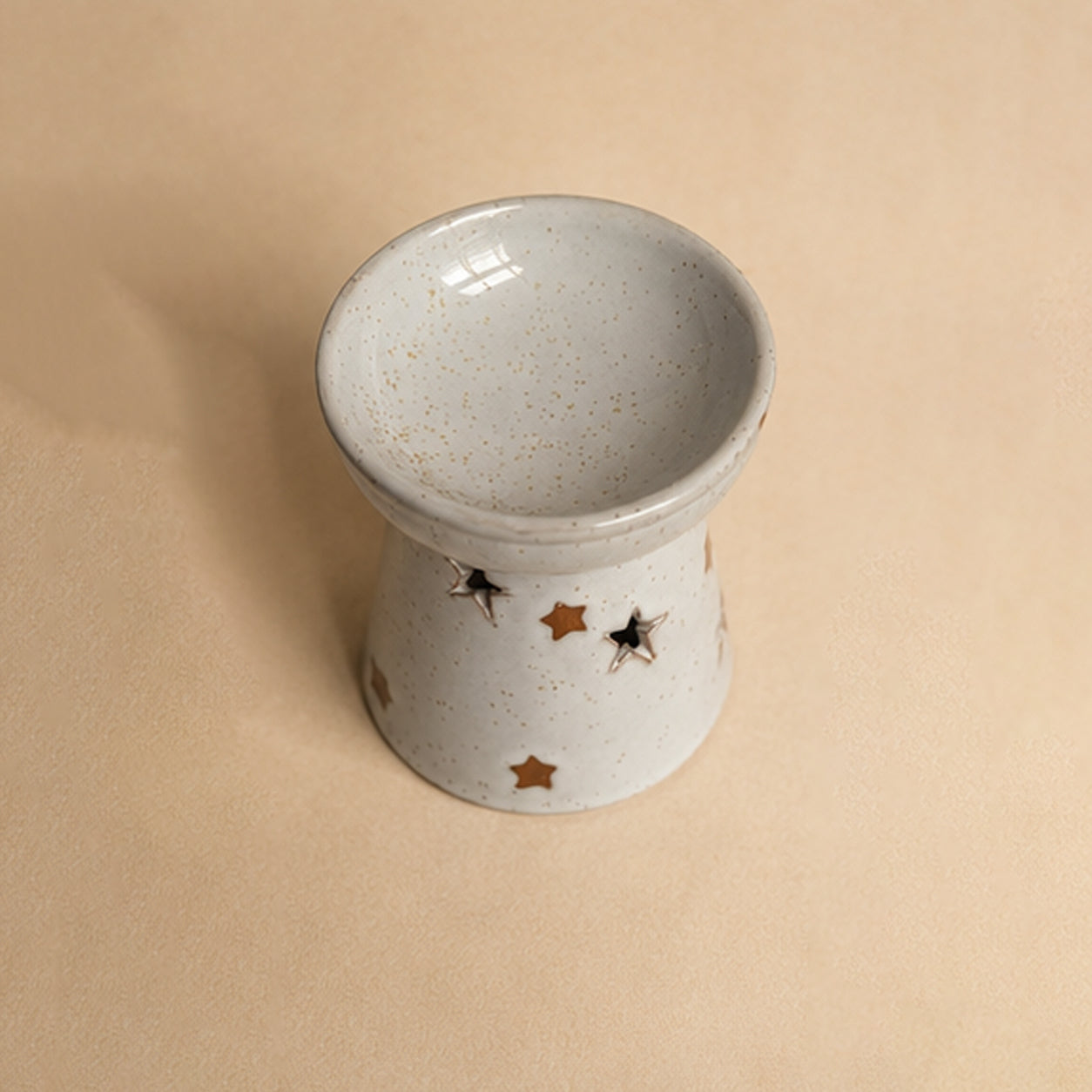 Empty ceramic wax burner with star designs on a beige background. Top down view. 