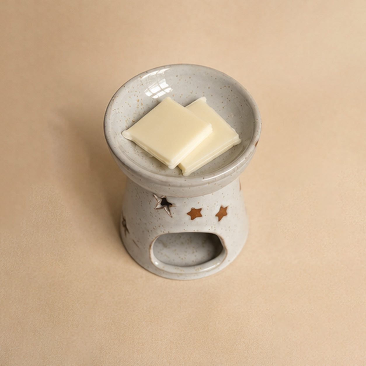 Ceramic wax burner with two squares of wax melt snap bar on a beige background. Top down view.