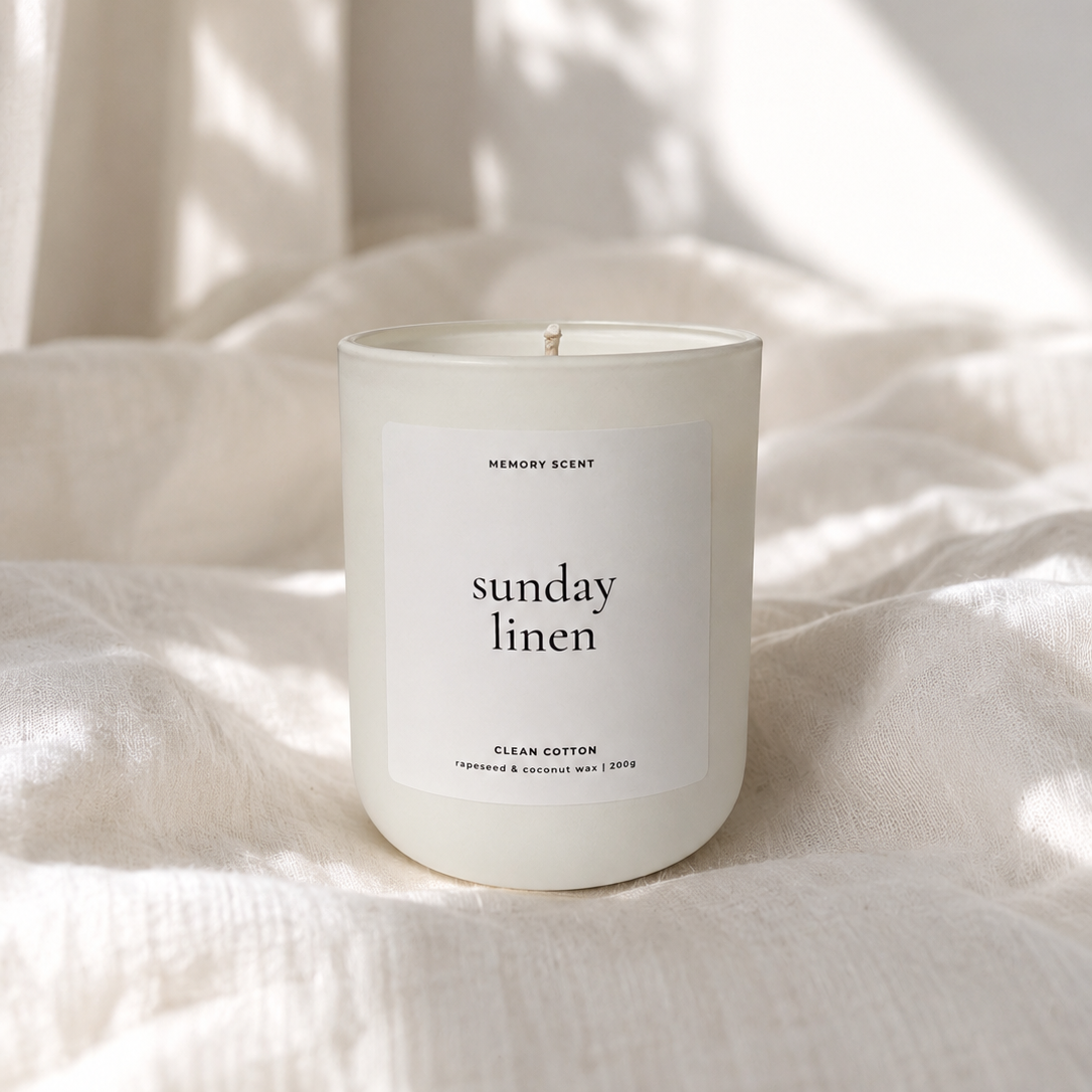 White candle labeled 'Sunday Linen' on a textured surface with soft lighting