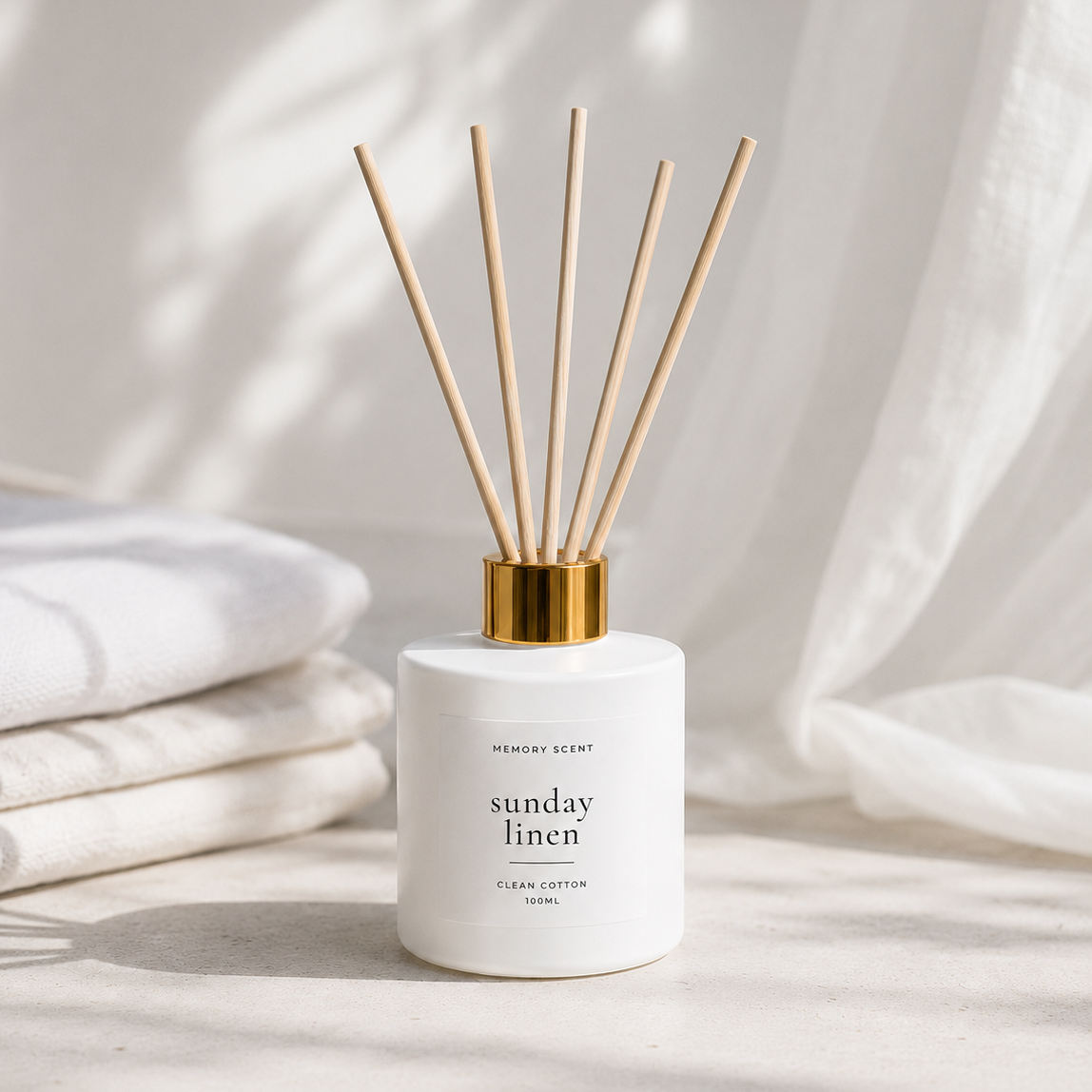 White jar, reed diffuser on a tabletop with sunday linen in the background. 