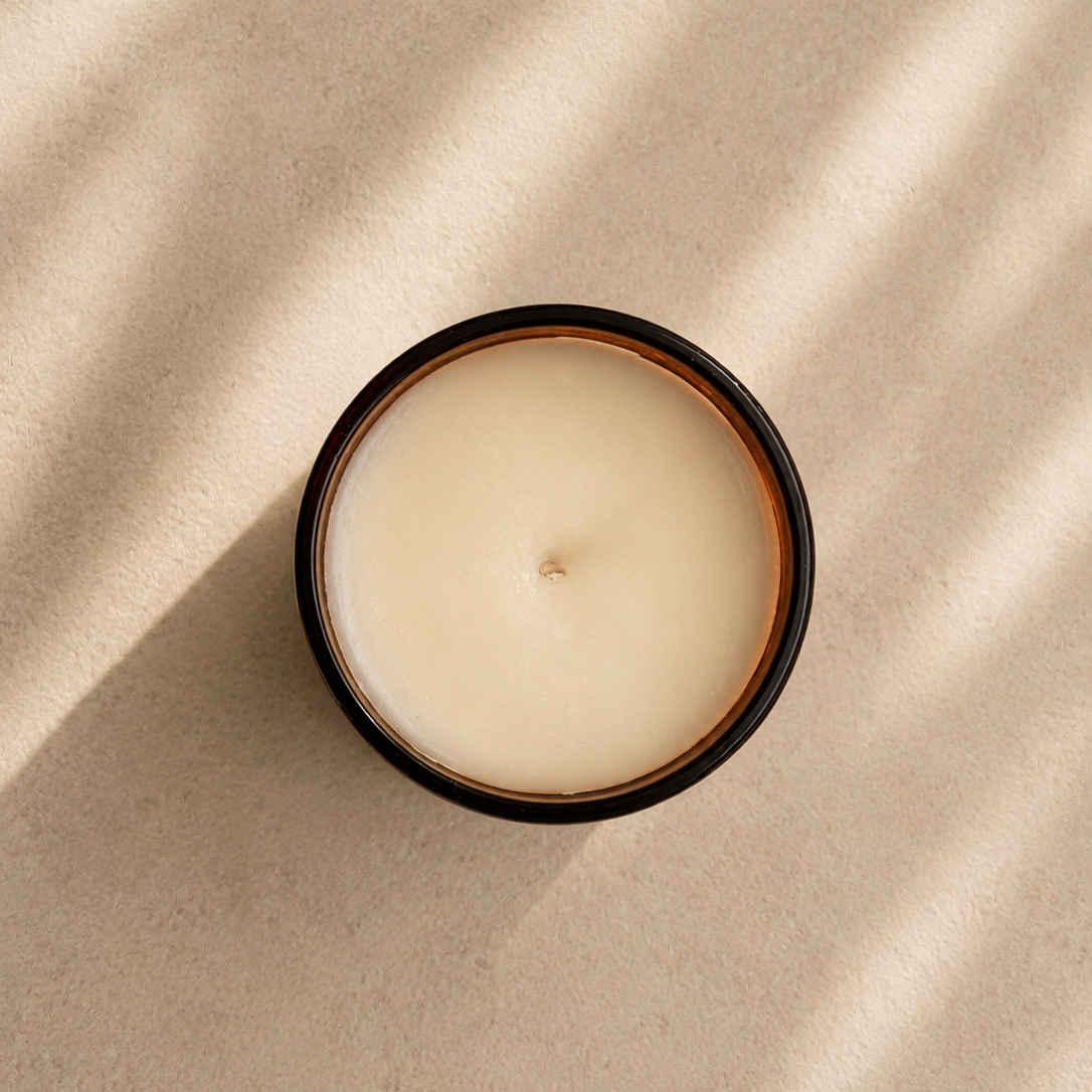Candle in a black container on a beige surface with soft shadows