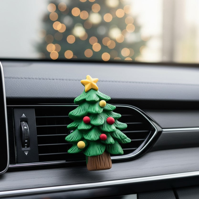 Christmas tree-shaped car air freshener on a car dashboard with blurred festive lights in the background.