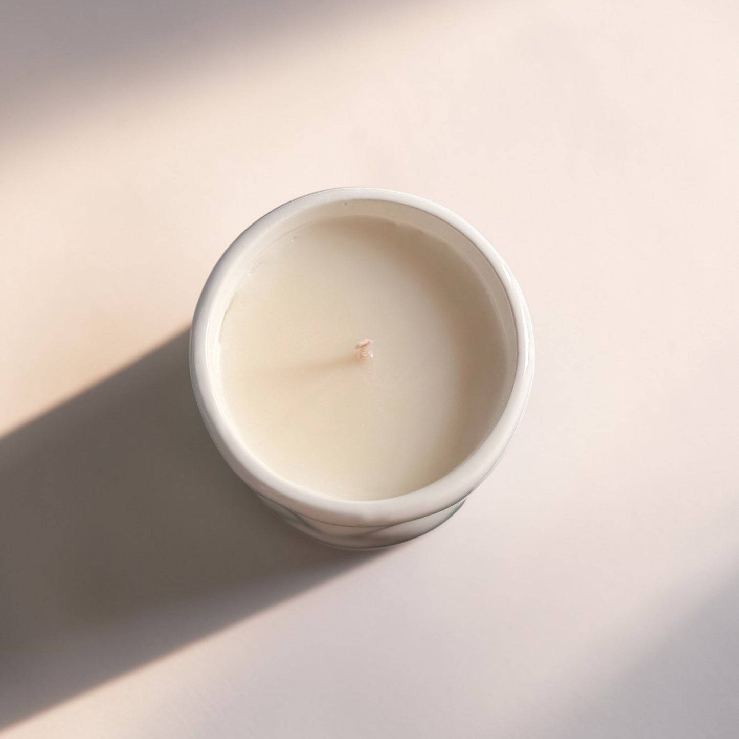 Top down view of candle in a white container on a light beige background