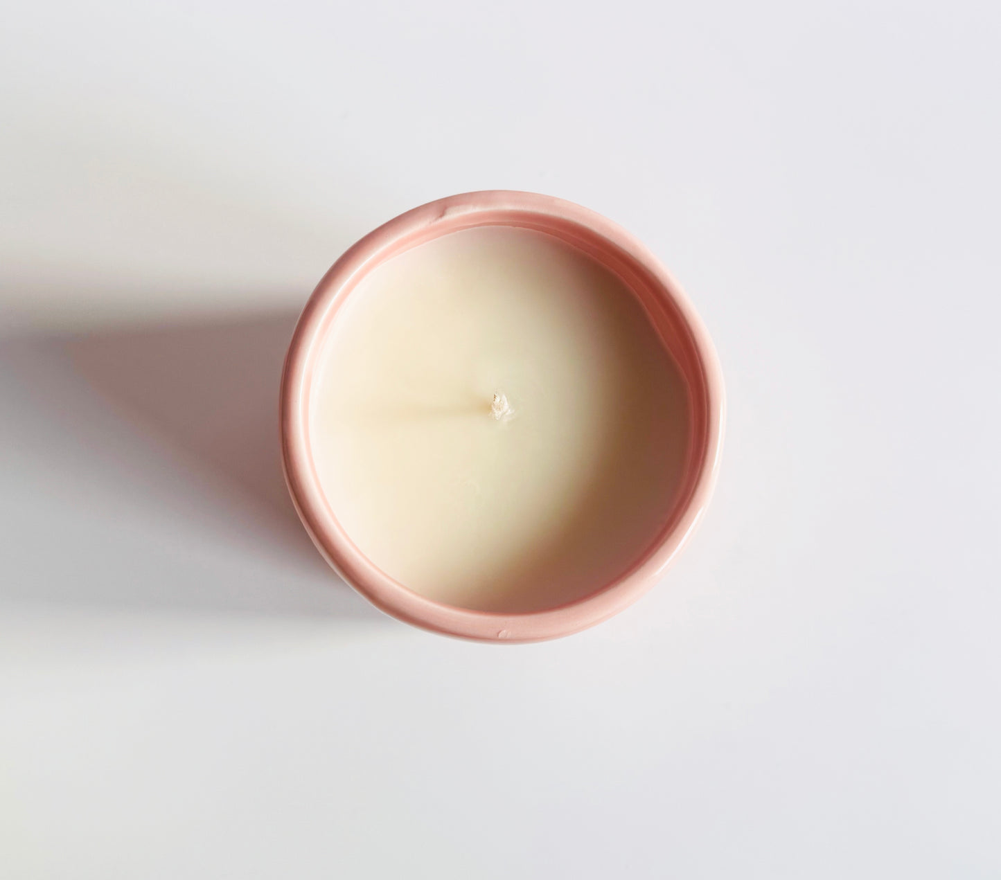 Top down view of a candle in a pink holder on a white background.