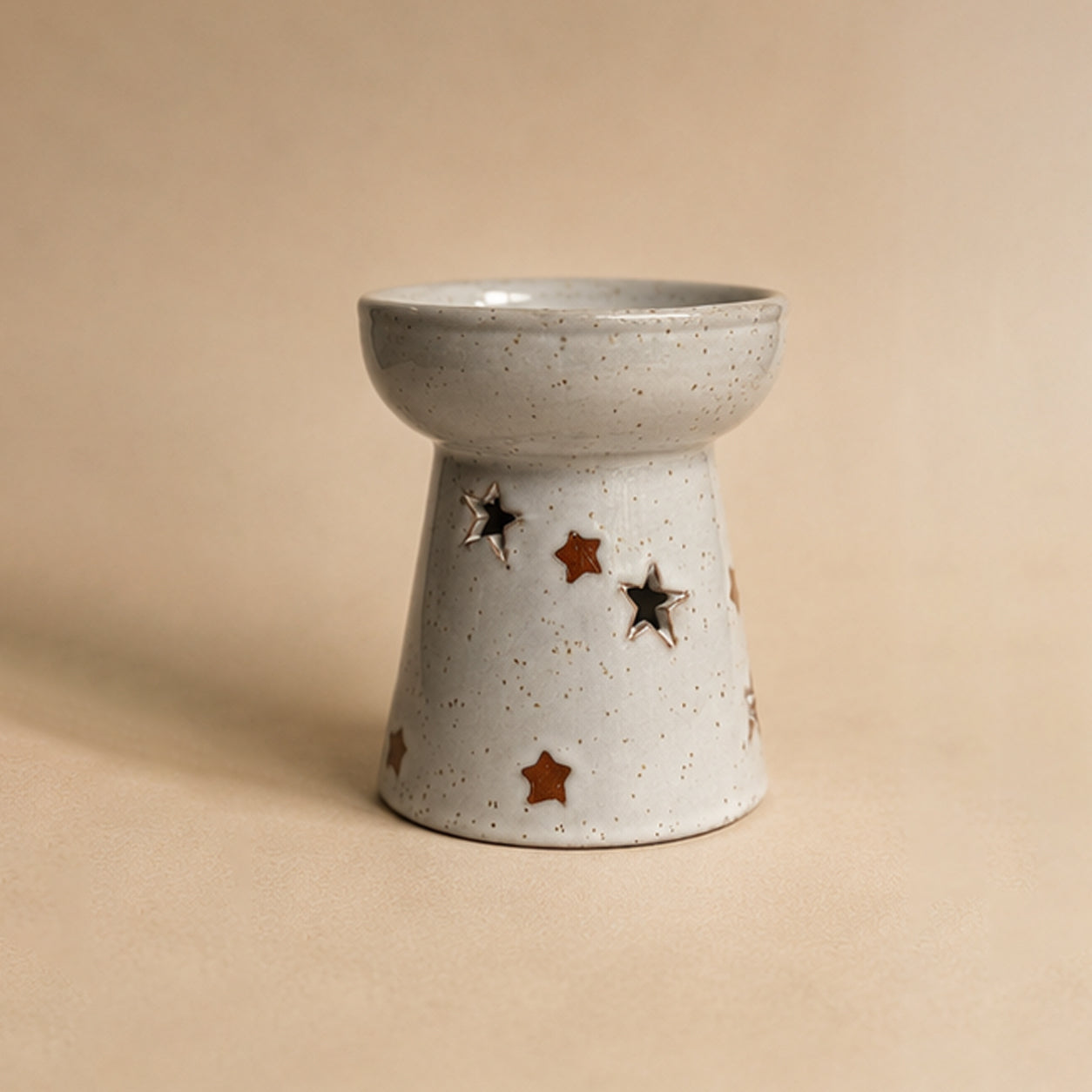 Ceramic wax burner with star designs on a beige background